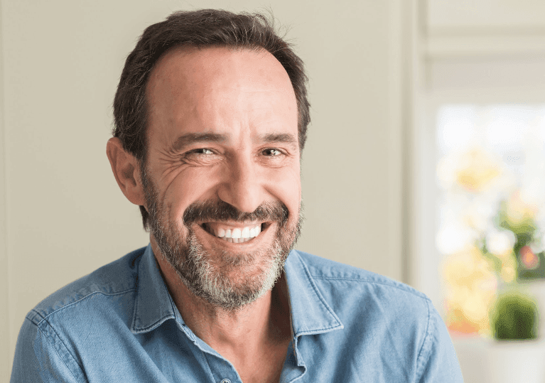 A cheerful man in a blue shirt and beard, representing CEREC technology with a warm smile.