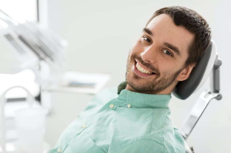 Man in a dental chair smiling, considering Invisalign braces for a straighter smile.